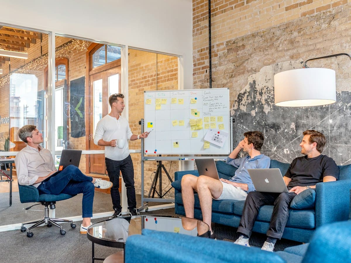 Team of engineers at laptops watching a colleague explain an architecture on a whiteboard