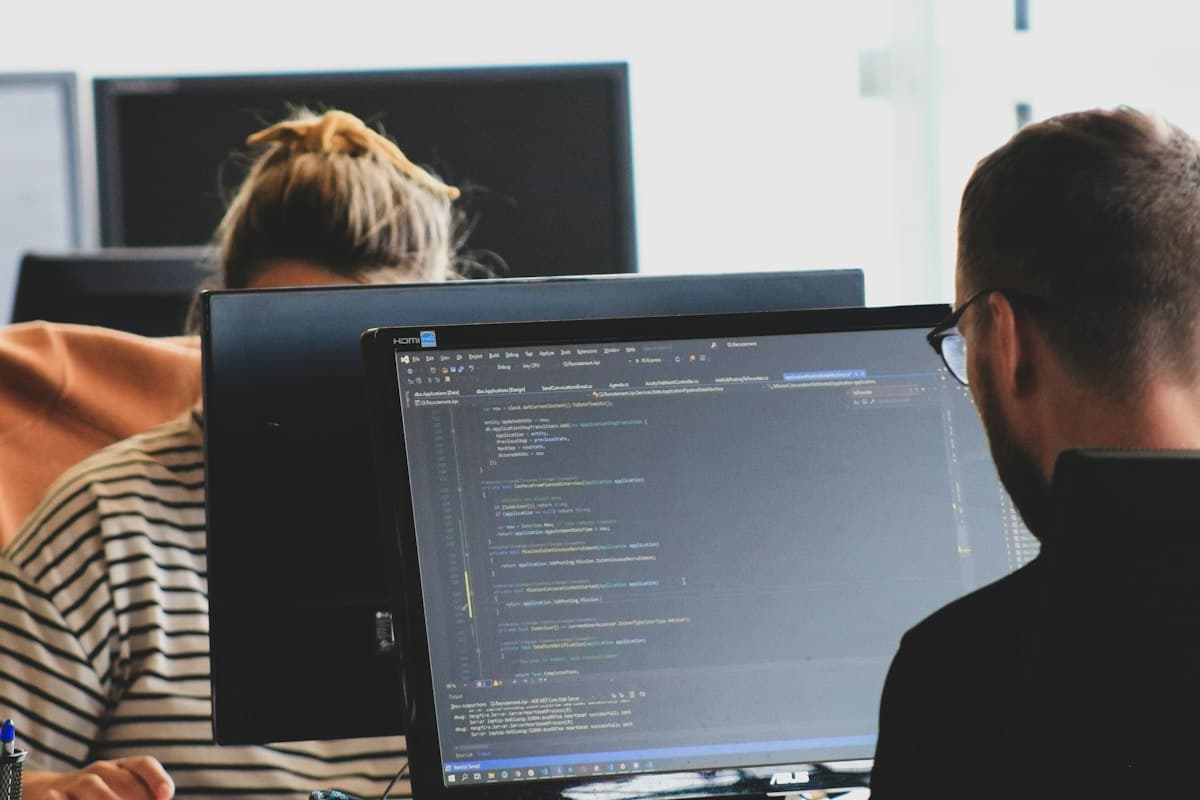 Two engineers working on integration code at monitors in a bright office, representing the engineering work of embedding AI agents into enterprise applications