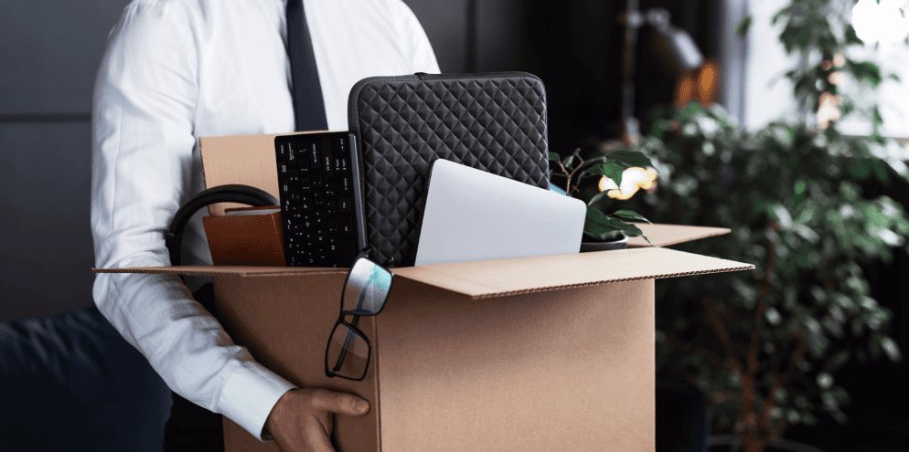 The image shows a professional with a box with his work things, symbolizing it turnover.