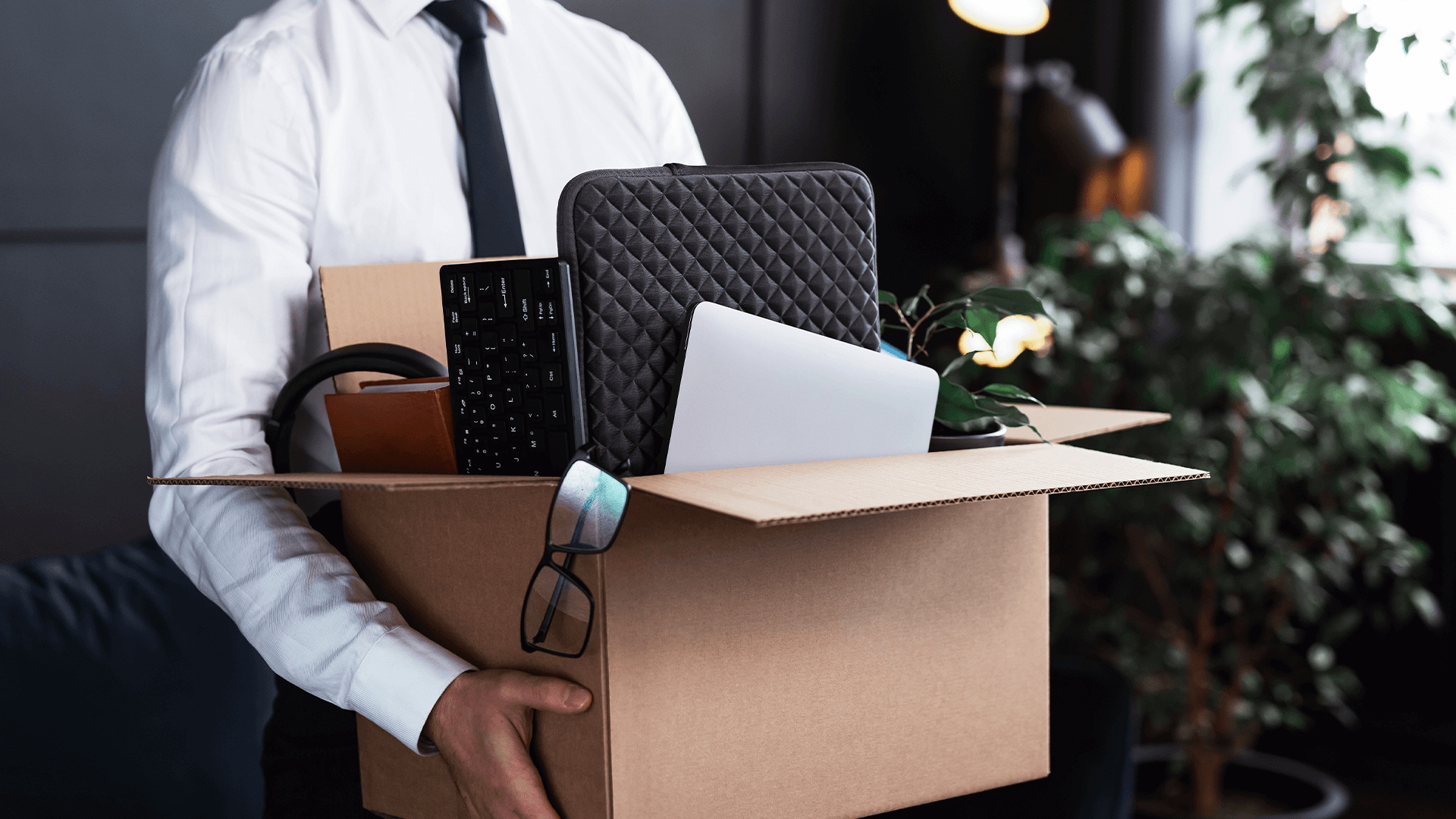 The image shows a professional with a box with his work things, symbolizing it turnover.